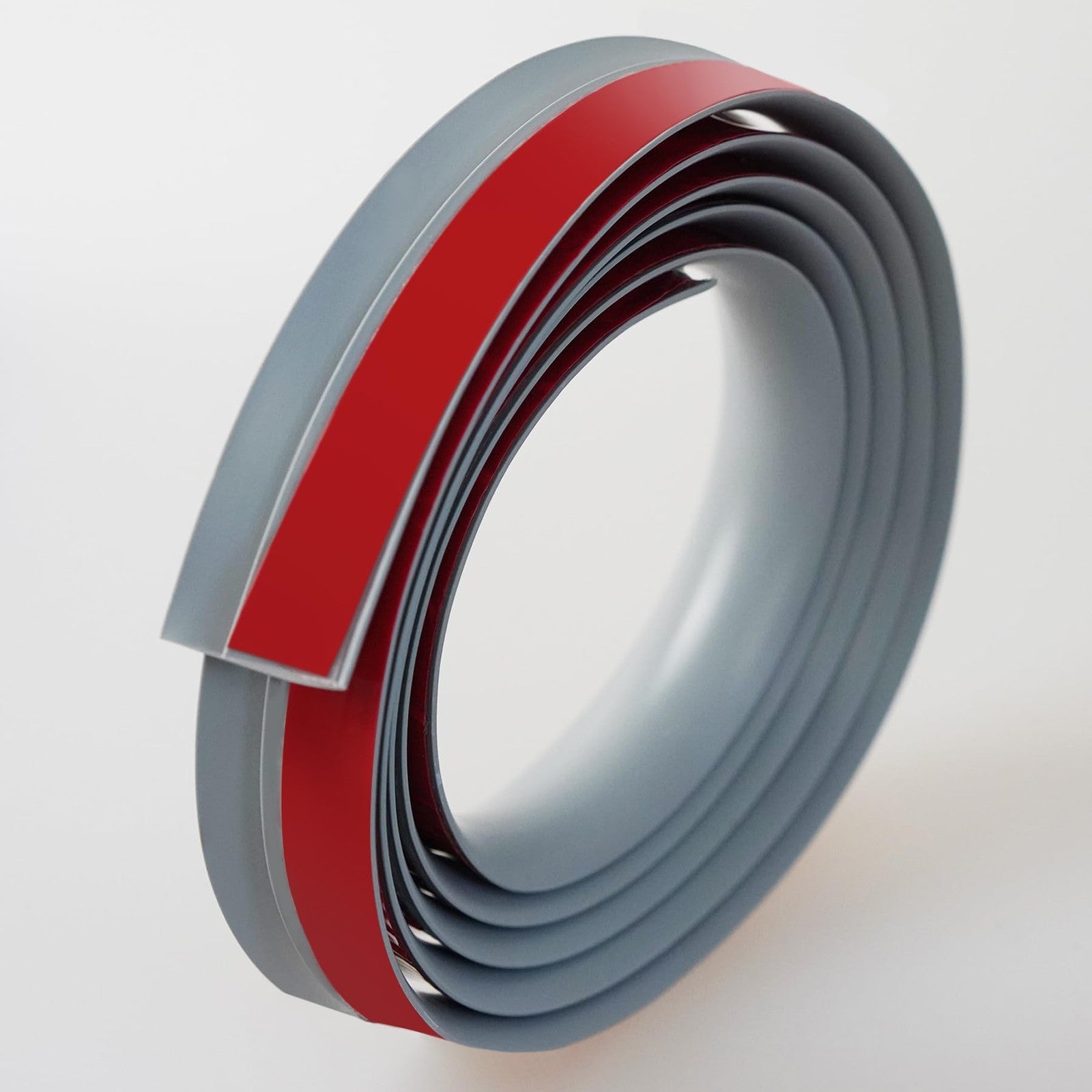 Trimold grey self-adhesive carpet to tile floor transition strip showing adhesive backing and smooth edging for seamless flooring transition.