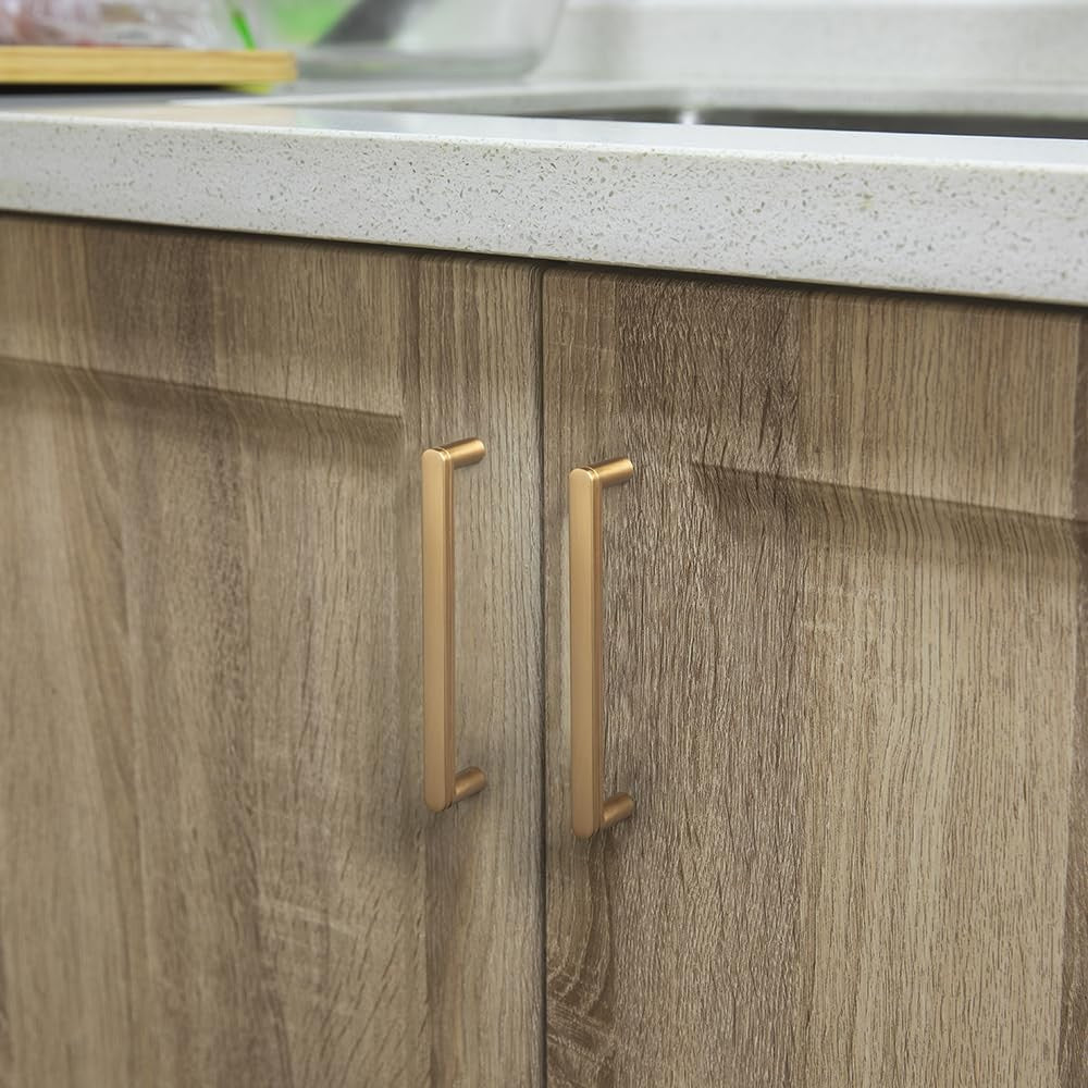 Goo-Ki 6-pack 5-inch champagne bronze cabinet pull handles with decorative grooved T design on a cabinet door.