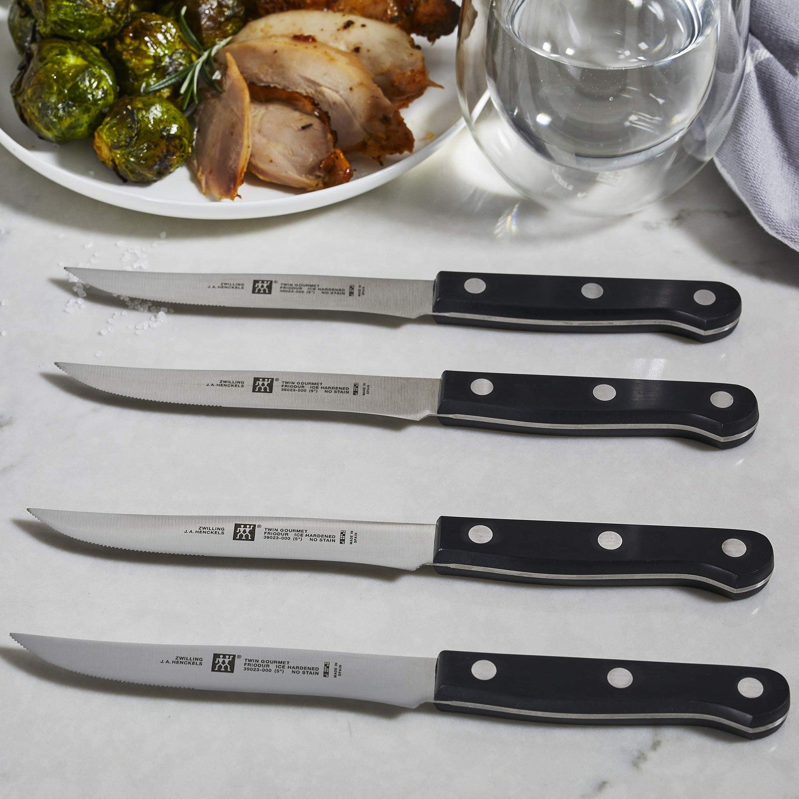 Set of four ZWILLING TWIN Gourmet steak knives with stainless steel blades and ergonomic handles for precise cutting.