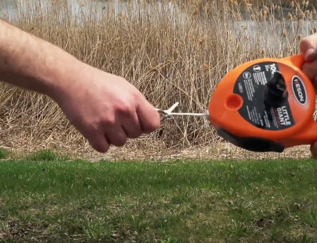 Keson G130 giant chalk line reel with 130ft length and 24oz chalk capacity, shown in use for outdoor marking and measuring tasks.