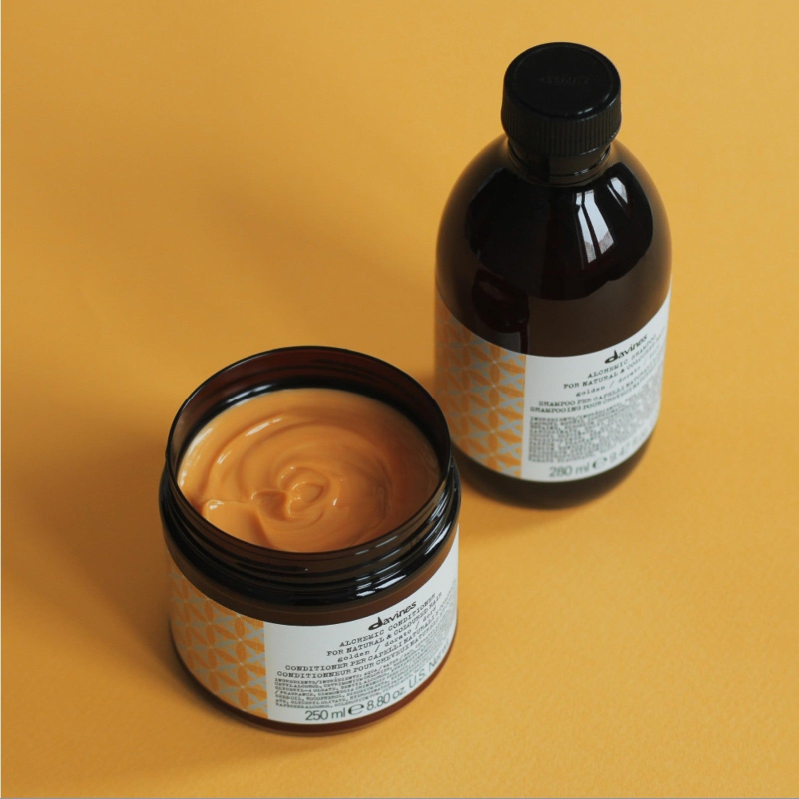 Davines Alchemic Conditioner Golden for blonde hair, color-depositing cream with golden hue, in a tub with product visible.