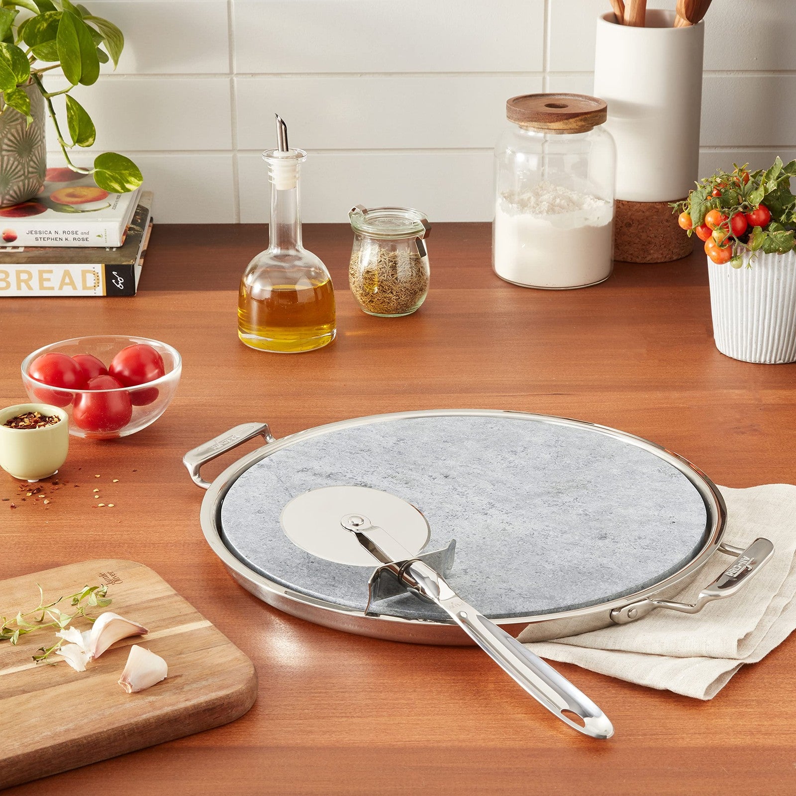 All-Clad 13-inch stainless steel and soapstone pizza stone for oven and broiler, shown with a pizza ready to bake
