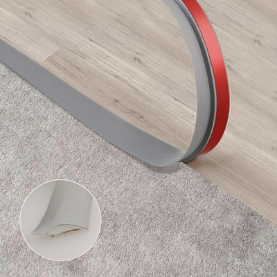 Trimold grey self-adhesive carpet to tile floor transition strip edging showing smooth, seamless connection between carpet and tile surfaces.