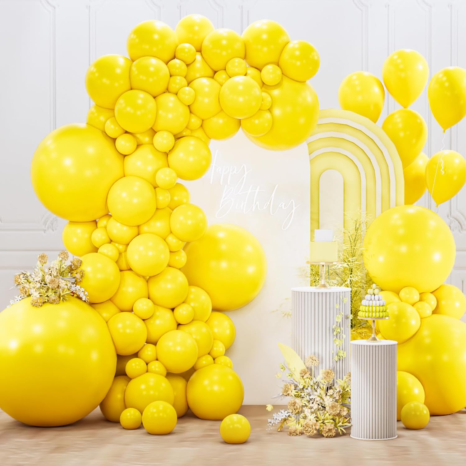 Yellow balloon arch with decorative elements on a wooden floor against a white wall.