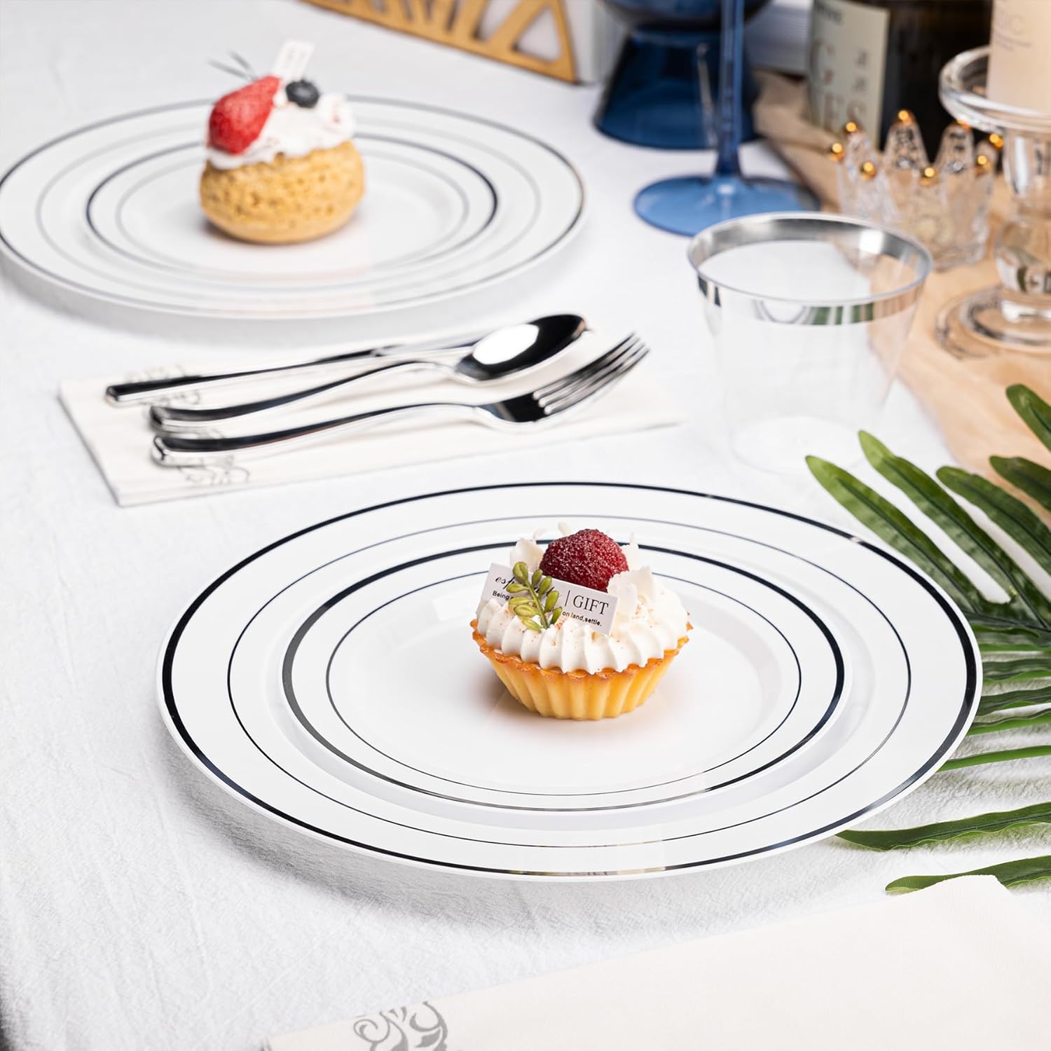 N9R 700-piece silver disposable dinnerware set for 100 guests, includes white plastic plates, cups, and utensils arranged on a table.