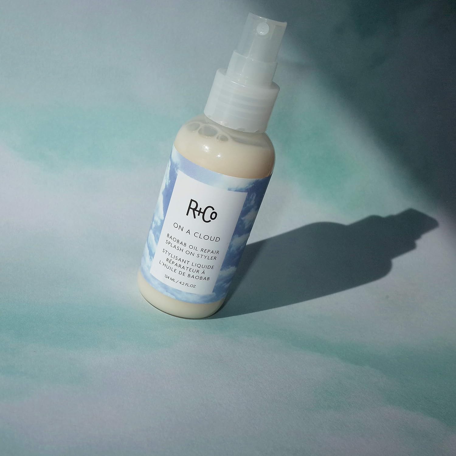 R+Co On A Cloud Baobab Oil Repair Splash on styler bottle, 124 ml, featuring sleek packaging and product label detail