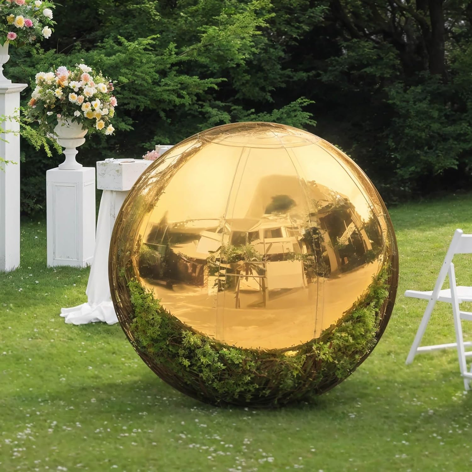 Gold reflective sphere on grass with floral arrangements and white chairs in the background