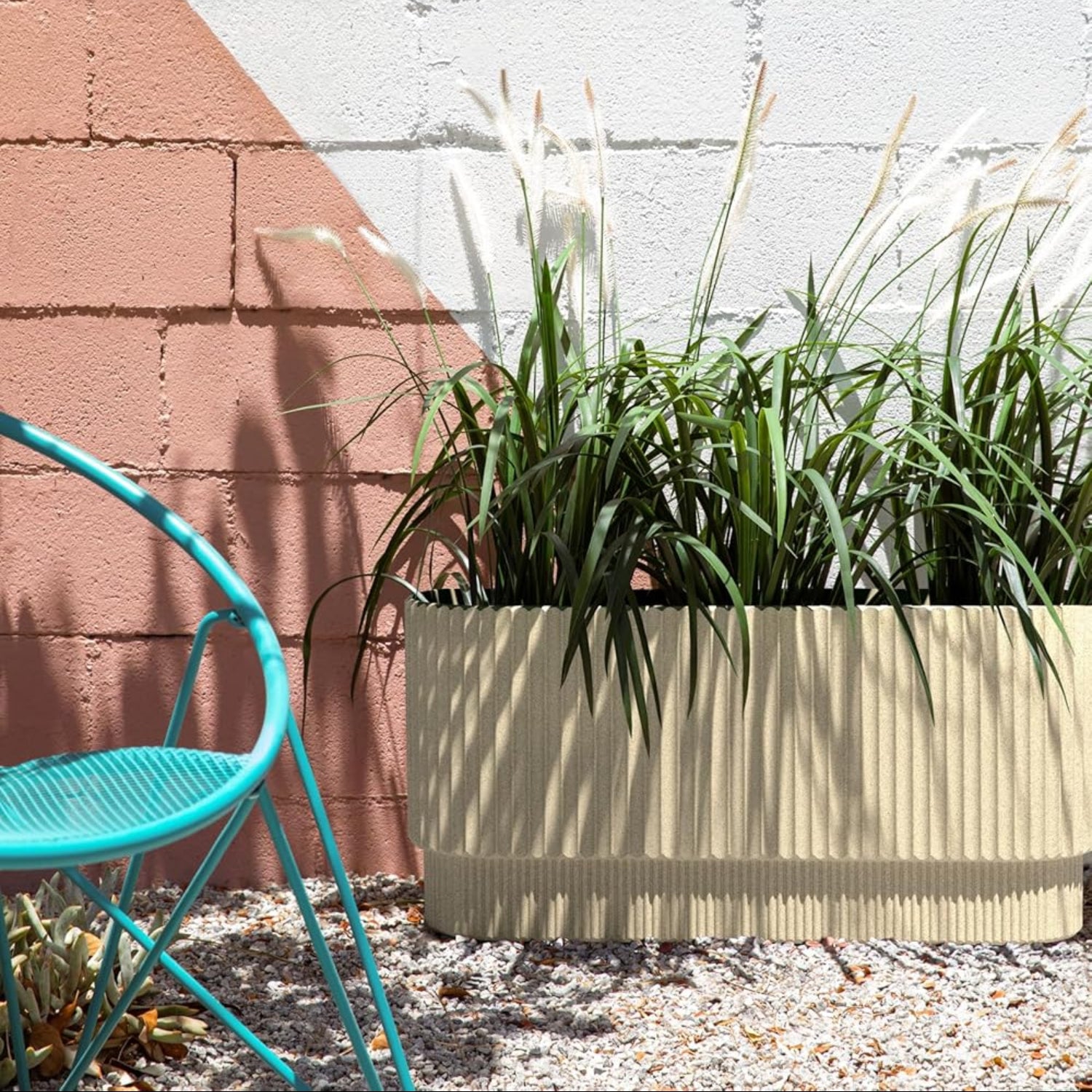 Beige planter with green plants against a white wall and red brick wall.