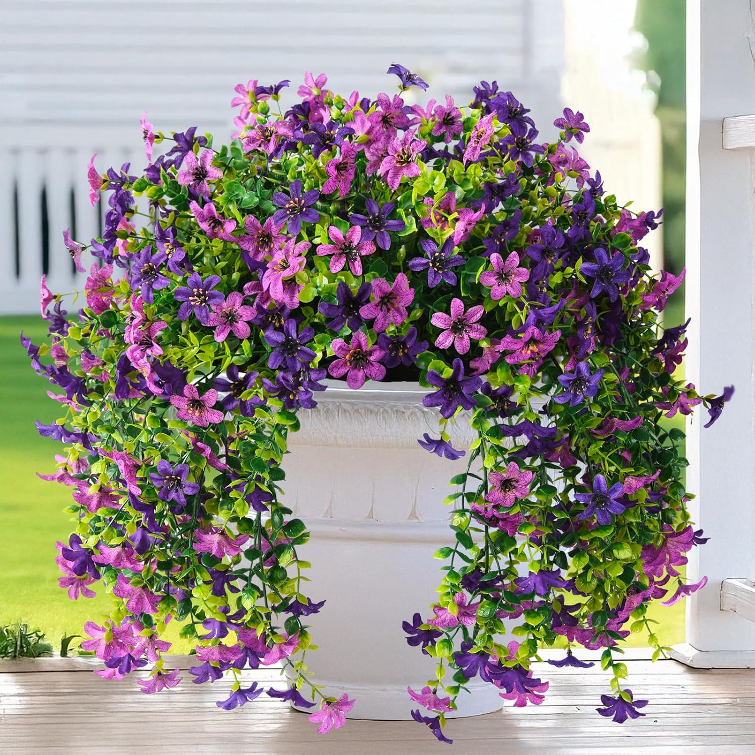 Artificial flower arch with purple and pink flowers in front of a white building.